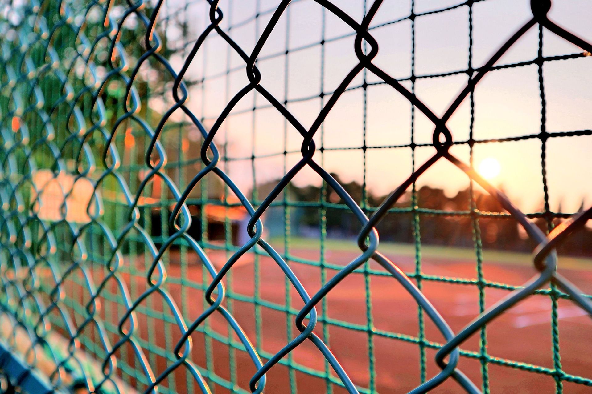 Close-up view of a chain link fence with a sunset over a sports field, creating a serene atmosphere.